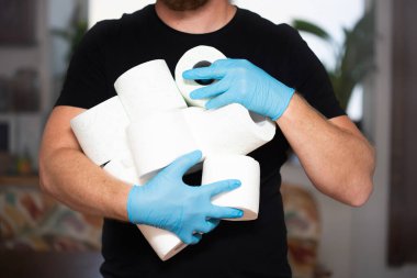 İnsanlar koronavirüs salgınından dolayı evdeki karantina için tuvalet kağıdı stokluyorlar. Adamın elinde bir sürü tuvalet kağıdı var..