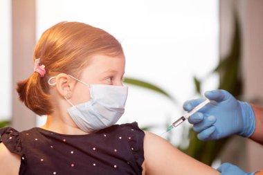 Çocuklar aşılama konsepti. Doktor yüz maskesi takan küçük bir kızın koluna aşı yapıyor..