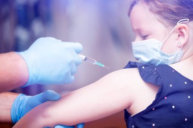 Çocuklar aşılama konsepti. Doktor yüz maskesi takan küçük bir kızın koluna aşı yapıyor..