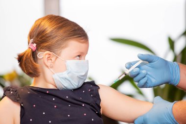 Çocuklar aşılama konsepti. Doktor yüz maskesi takan küçük bir kızın koluna aşı yapıyor..