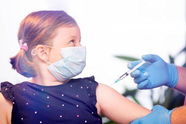 Çocuklar aşılama konsepti. Doktor yüz maskesi takan küçük bir kızın koluna aşı yapıyor..