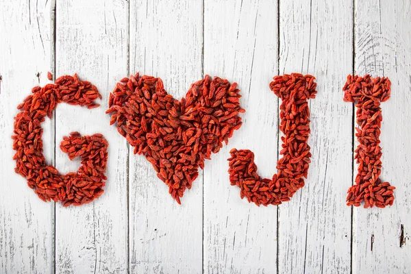 Bayas de Goji como corazón y letras en una vieja mesa de madera blanca . —  Fotos de Stock