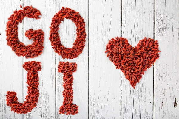 Bacche di Goji come un cuore e lettere su vecchio tavolo di legno bianco . — Foto Stock