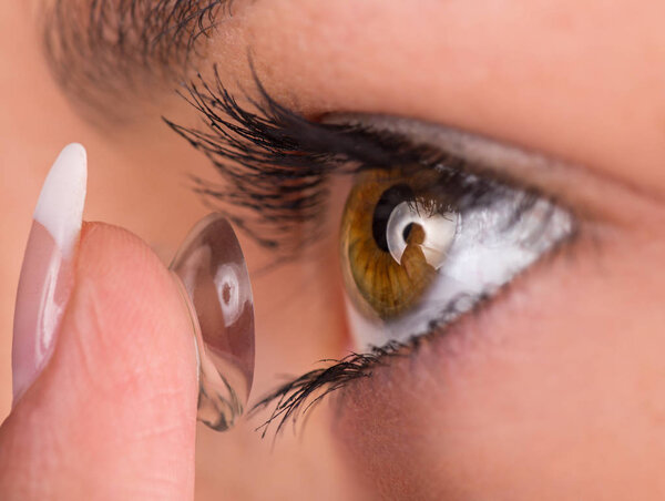 Young woman putting contact lens in her eye.