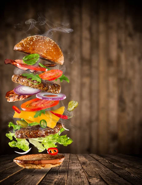 Grande hambúrguer saboroso com ingredientes voadores . — Fotografia de Stock