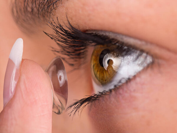Young woman putting contact lens in her eye.