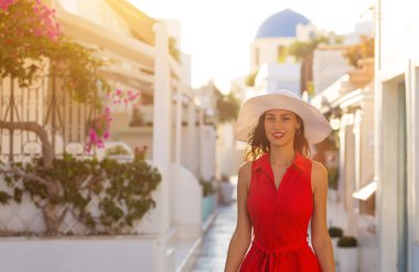 Santorini travel tourist brunette woman in red dress visiting famous white Oia village. clipart