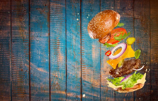 Grande hambúrguer saboroso com ingredientes voadores . — Fotografia de Stock