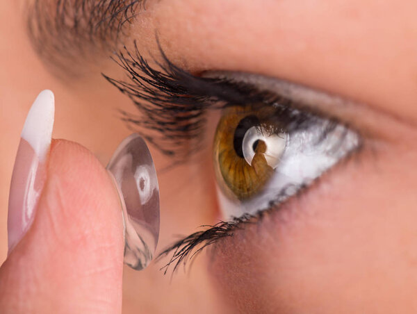 Young woman putting contact lens in her eye.