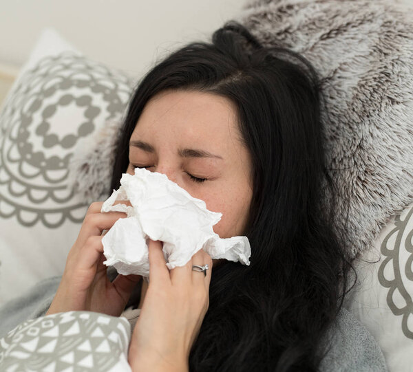 Young woman having flu, blowing her nose.