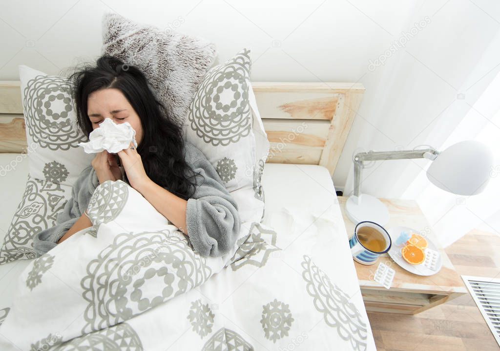 Young woman having flu, blowing her nose.