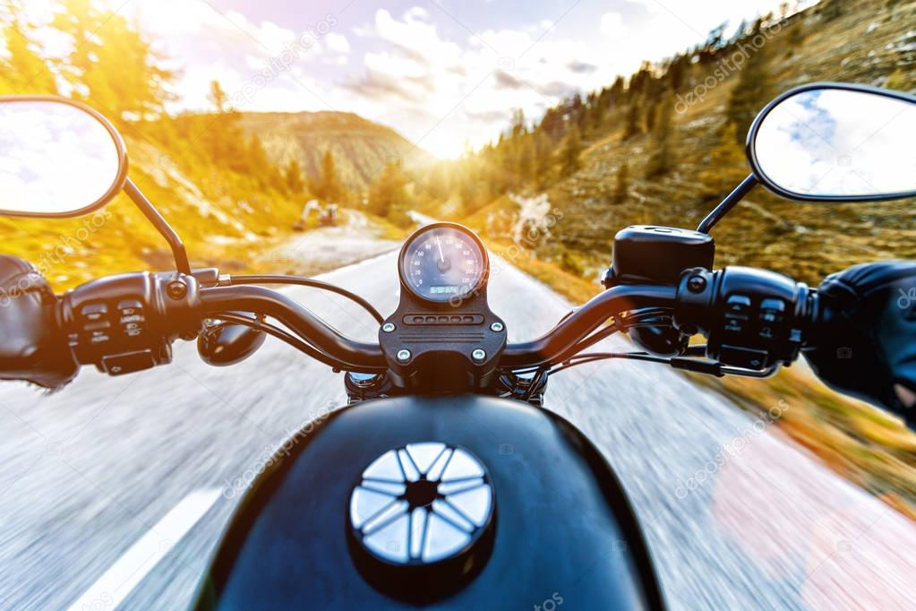 Motorcycle driver riding in Alpine highway, handlebars view, Austria, Europe.