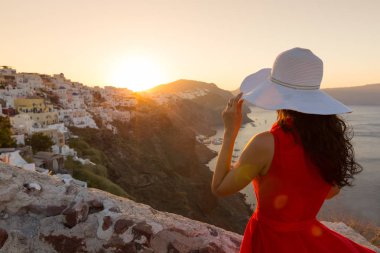 Santorini seyahat ediyor. Kırmızı elbiseli esmer kadın ünlü beyaz Oia köyünü ziyaret ediyor..