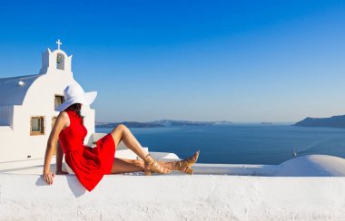 Santorini seyahat ediyor. Kırmızı elbiseli esmer kadın ünlü beyaz Oia köyünü ziyaret ediyor..