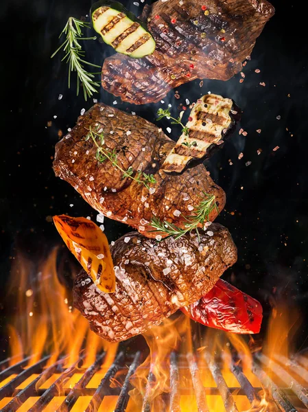 Kettle grill with hot briquettes, cast iron grate and tasty beef steaks flying in the air. — Stock Photo, Image