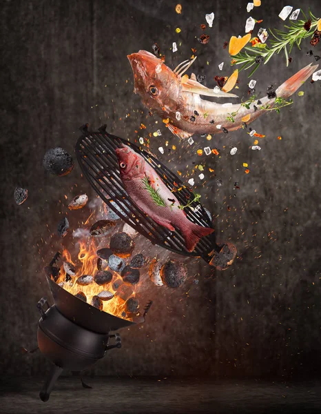 Grelha de chaleira com briquetes quentes, grelha de ferro fundido e peixes marinhos saborosos voando no ar . — Fotografia de Stock