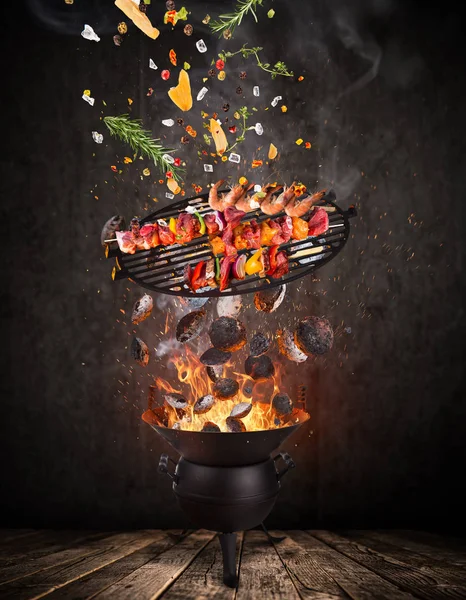 Grelha de chaleira com briquetes quentes, grelha de ferro fundido e espetos saborosos voando no ar . — Fotografia de Stock