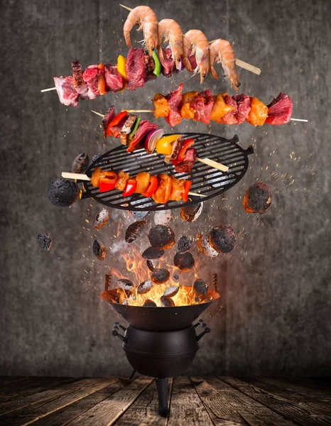 Kettle grill with hot briquettes, cast iron grate and tasty skewers flying in the air.