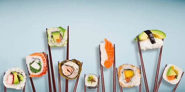Traditional japanese sushi pieces placed between chopsticks, separated on light blue pastel background.