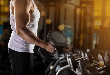 Kaslı genç adam dumbbells ile pazı için kilo egzersiz yapıyor