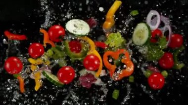 Siyah arka planda patlayan su damlacıkları olan taze sebzeler..