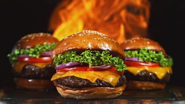 Chutný cheeseburger, ležící na staré dřevěné řezací desce s ohněm v pozadí. Super zpomalený pohyb