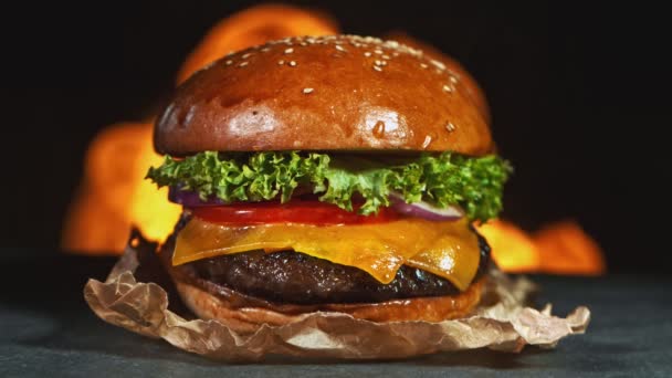 Savoureux cheeseburger, couché sur une planche à découper vintage en bois avec des flammes de feu en arrière-plan. Super ralenti — Video