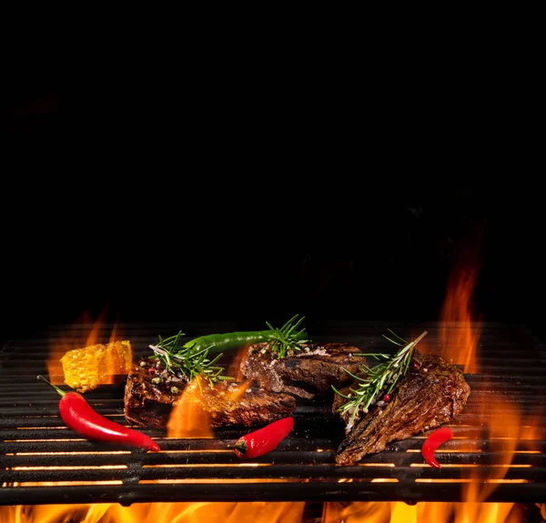 Bifes de carne saborosos voando acima grade de ferro fundido com chamas de fogo. — Fotografia de Stock