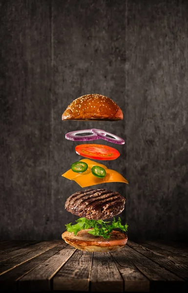 Smaczny hamburger z latania składników na ciemnym tle — Zdjęcie stockowe