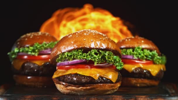 Sabrosa hamburguesa con queso, acostado en una tabla de cortar de madera vintage con llamas de fuego en el fondo. Super cámara lenta — Vídeo de stock