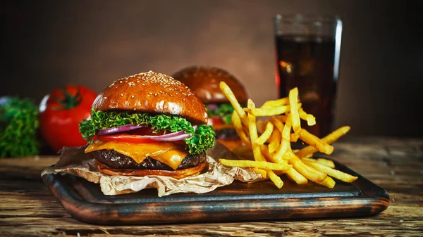 Frytki spadają obok cheeseburgera, leżącego na drewnianej desce do krojenia vintage. — Zdjęcie stockowe