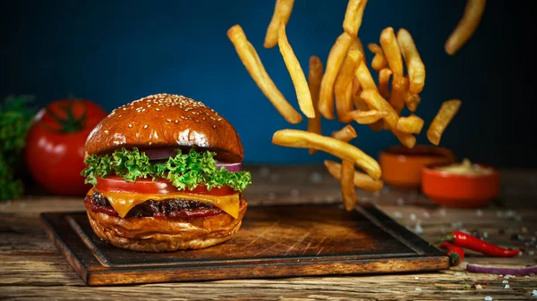 French fries fall next to cheeseburger, lying on vintage wooden cutting board.