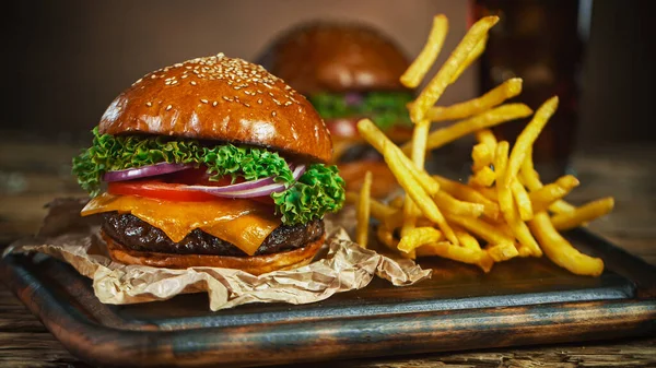 Pommes frites faller ved siden av cheeseburger, liggende på vintage treskjæringstavle. – stockfoto