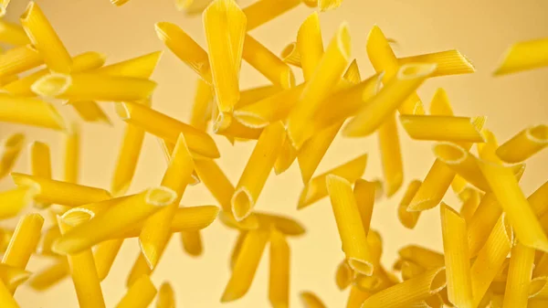 Freeze motion of flying uncooked italian pasta on golden background. — Stock Photo, Image