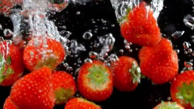 Siyah arka planda suyla patlayan çilekler..