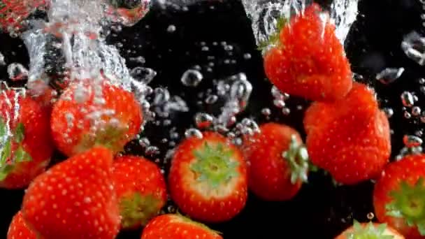 Exploderende aardbeien met water op een zwarte achtergrond. — Stockvideo
