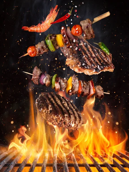 Tasty beef steaks and skewers flying above cast iron grate with fire flames. — Stock Photo, Image