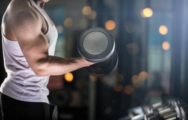 Kaslı genç adam dumbbells ile pazı için kilo egzersiz yapıyor