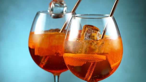 Ледяной кубик падает в стакан апельсинового коктейля. — стоковое видео