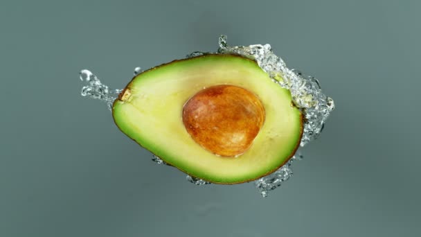 Super rallentamento girato di mezzo avocado con spruzzatura di acqua isolata su sfondo grigio — Video Stock