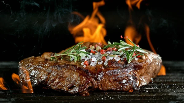 Tasty beef steak on cast iron grate with fire flames. — Stock Photo, Image