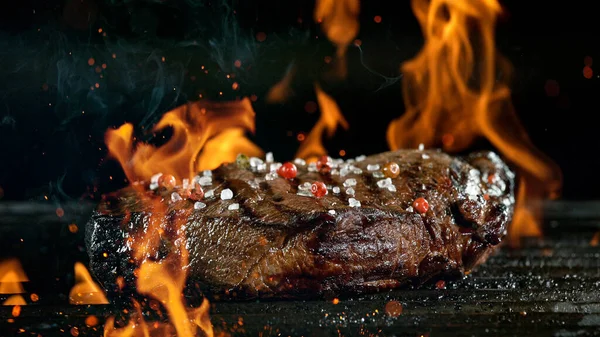 Lekkere biefstuk op gietijzeren rooster met vuurvlammen. — Stockfoto