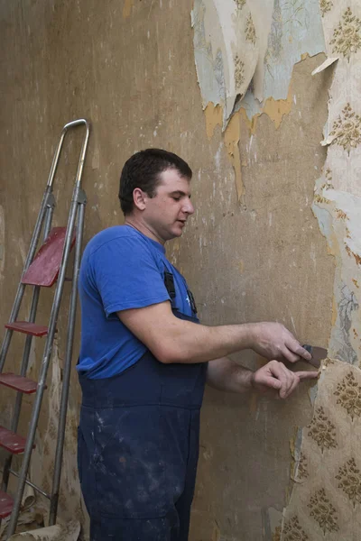 Ανακαίνιση Κατοικίας Άνδρας Εργαζόμενος Αφαιρεί Παλαιά Ταπετσαρία Από Ένα Τσιμεντένιο — Φωτογραφία Αρχείου