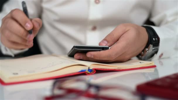 Businessman Using His Smartphone And Taking Notes In Diary. Close Up — Stock Video