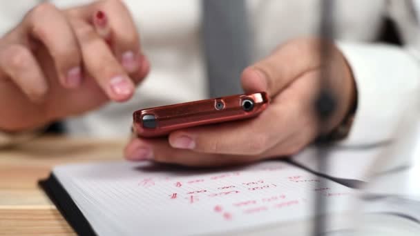 Affärsman med hjälp av sin mobiltelefon och ta anteckningar i anteckningar. Närbild — Stockvideo