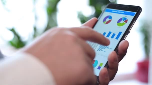 Ręka trzyma telefon komórkowy z wykres giełdowy i statystyk finansowych na ekranie — Wideo stockowe