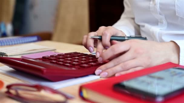 Mujer comerciante está monitoreando las estadísticas en la calculadora. Y escribe datos de stock en papel — Vídeo de stock