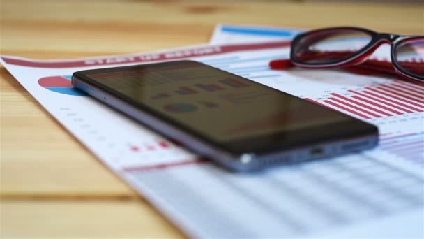 Modern Working Place. Mobile Phone, Pen, Glasses And Paper With Charts On Table — Stock Video