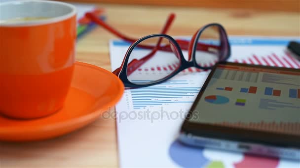 Мобильный телефон, стаканы, деловой отчет и чашка кофе на столе — стоковое видео