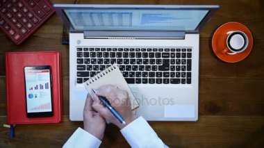 İşadamı kullanarak dizüstü bilgisayar ve yazar Menkul Kıymetler Borsası istatistik olarak not defteri. Yukarıdan görüntülemek